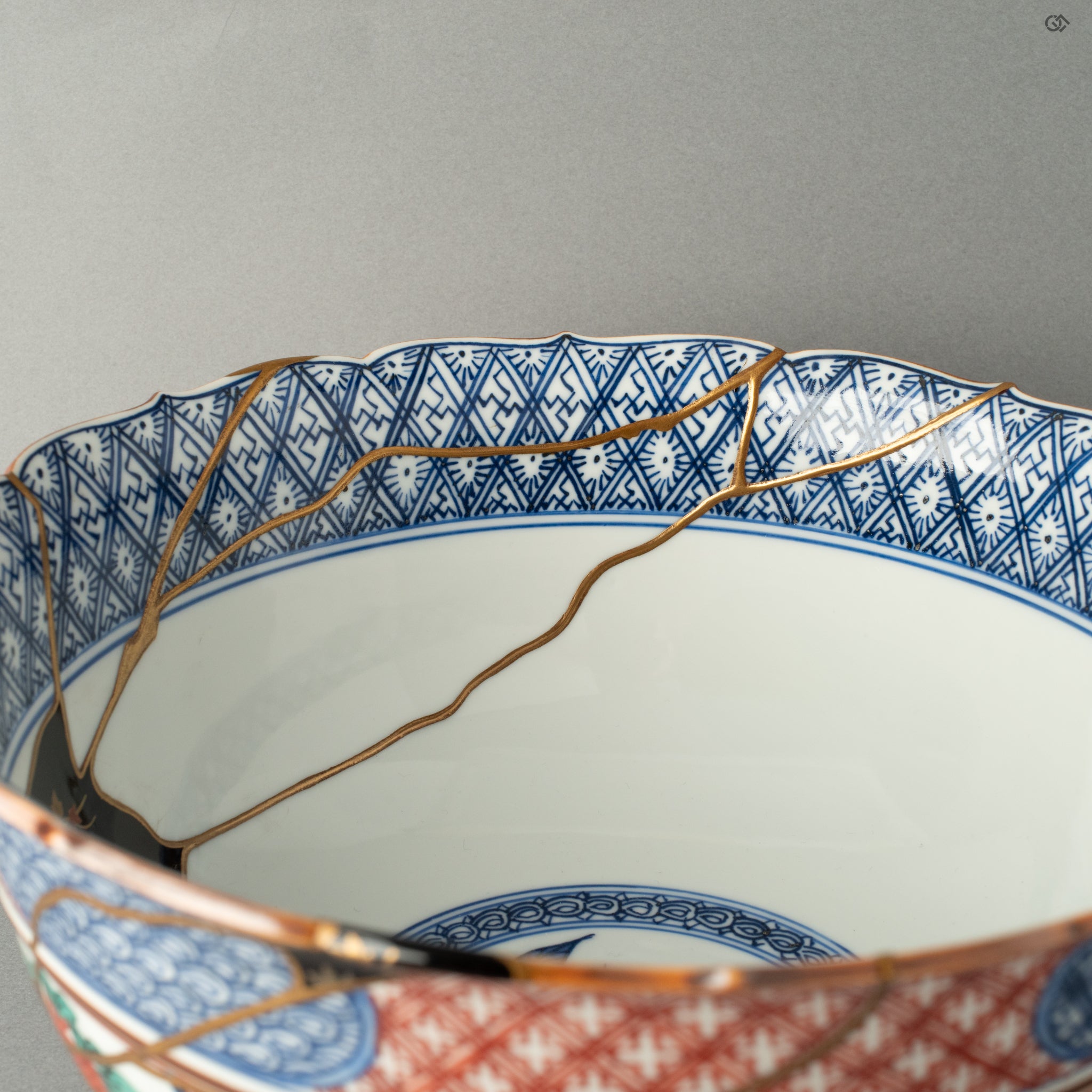 An intimate detail showing how a wide, brilliant gold Kintsugi line respectfully navigates the original hand-painted blue-and-white Shonzui motifs, bridging centuries of Japanese artistry.