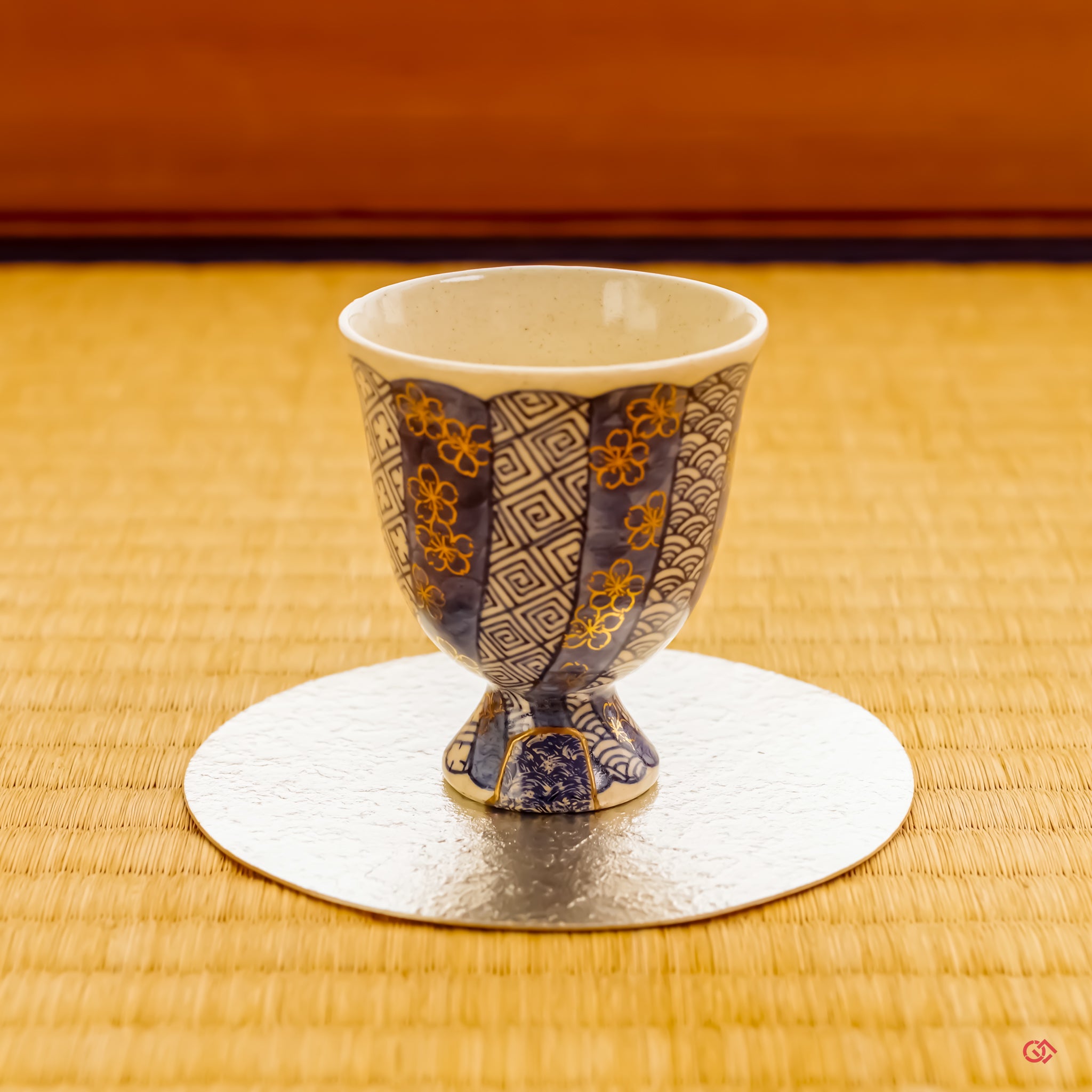 A beautifully restored Kintsugi vessel from Kyoto, resting on a lustrous, thin pewter coaster atop a traditional tatami mat. The scene captures a serene harmony between historic craft and modern elegance.