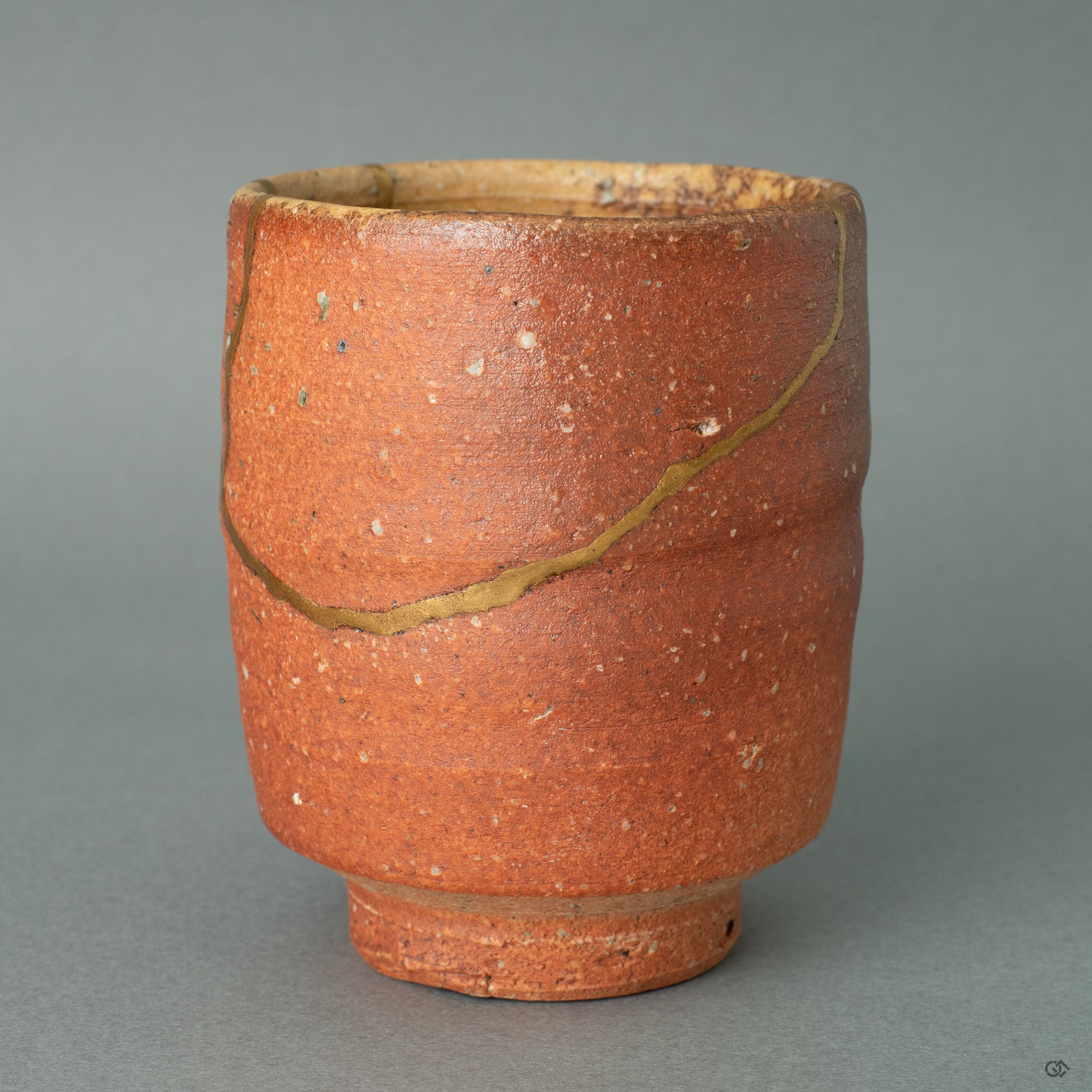 A close-up view of a luminous 24k gold Kintsugi line flowing over the warm, unglazed surface of the Shigaraki clay, highlighting the contrast between refined metal and natural earth.