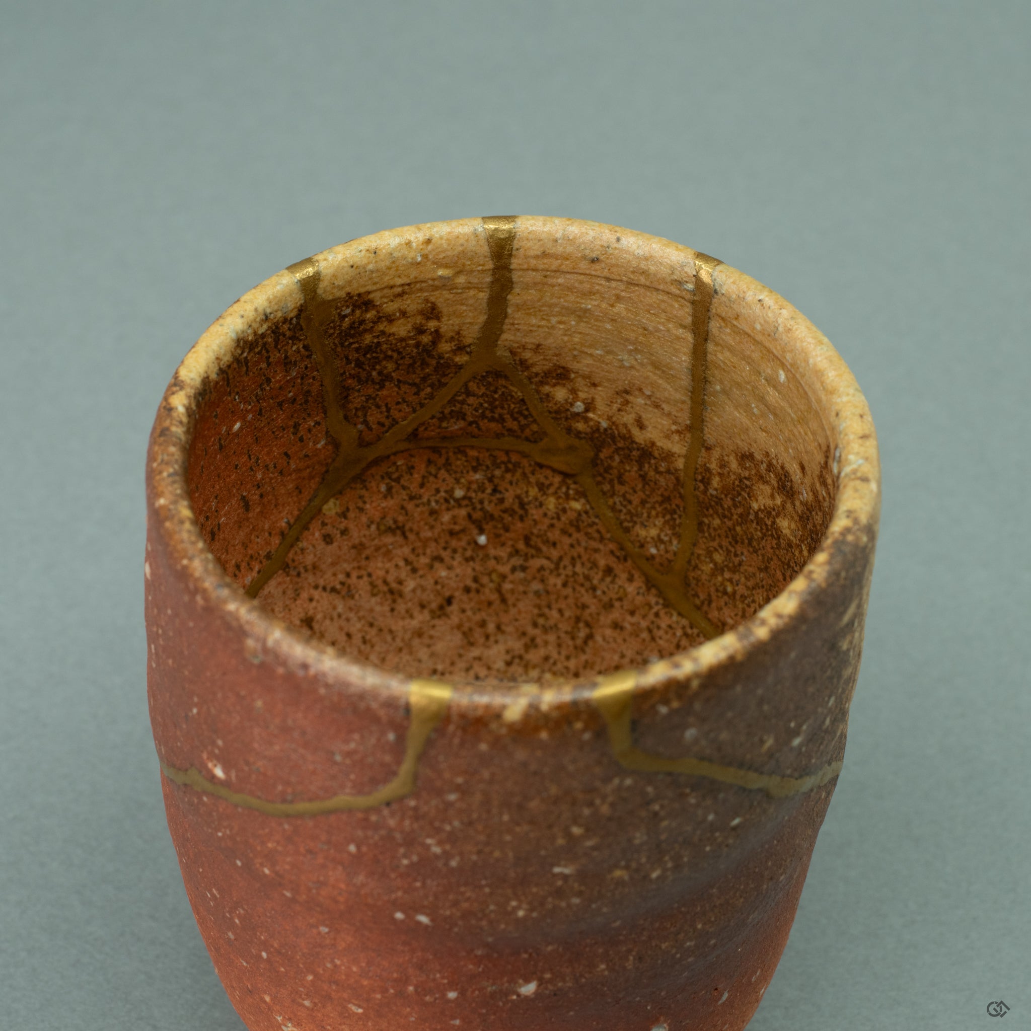 An intimate close-up focused on the point where the rich texture of the 24k gold maki-e meets the gritty, mineral surface of the Shigaraki ware. The seamless joinery is a testament to the artisan's meticulous skill, celebrating the fusion of precious metal and ancient clay.