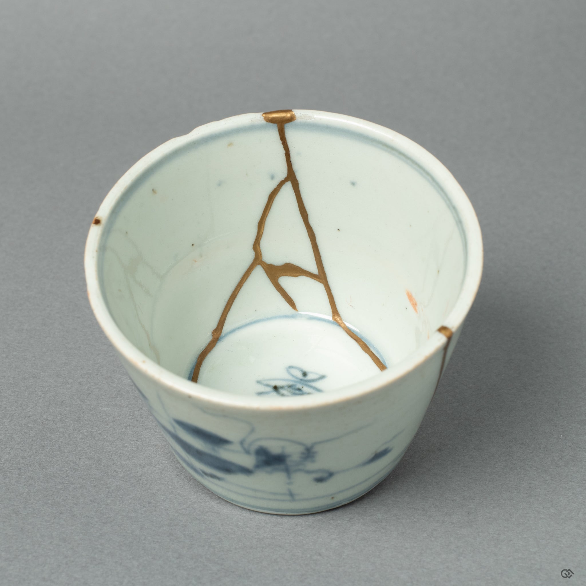 A detailed close-up of a 24k gold Kintsugi line on the antique Ko-Imari porcelain. The precision reflects the meticulous skill honed through the restoration of sacred sculptures.