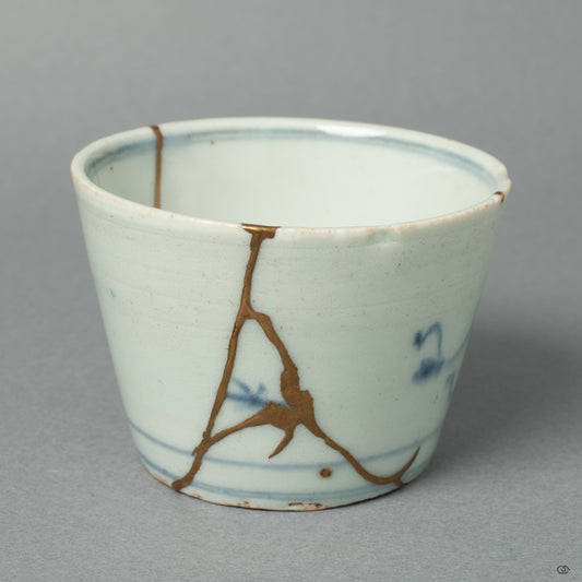 An antique Ko-Imari porcelain ochoko, its historic form reborn with 24k gold Kintsugi by a conservator of sacred Buddhist art. The repair respects the vessel's heritage while adding a new, precious history.