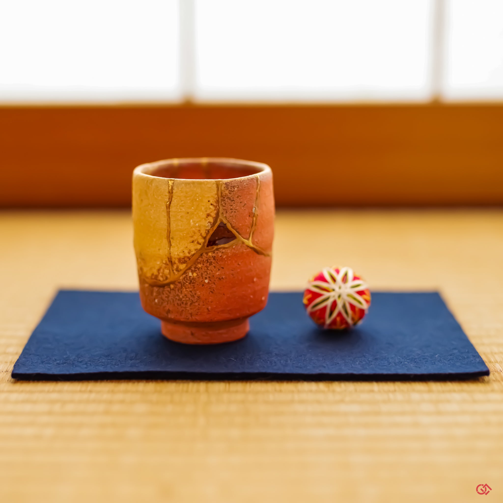 A beautifully restored Kintsugi teacup resting on a lustrous, thin pewter coaster atop a traditional tatami mat. The tranquil scene captures a harmony between historic Japanese craft and refined, contemporary elegance.