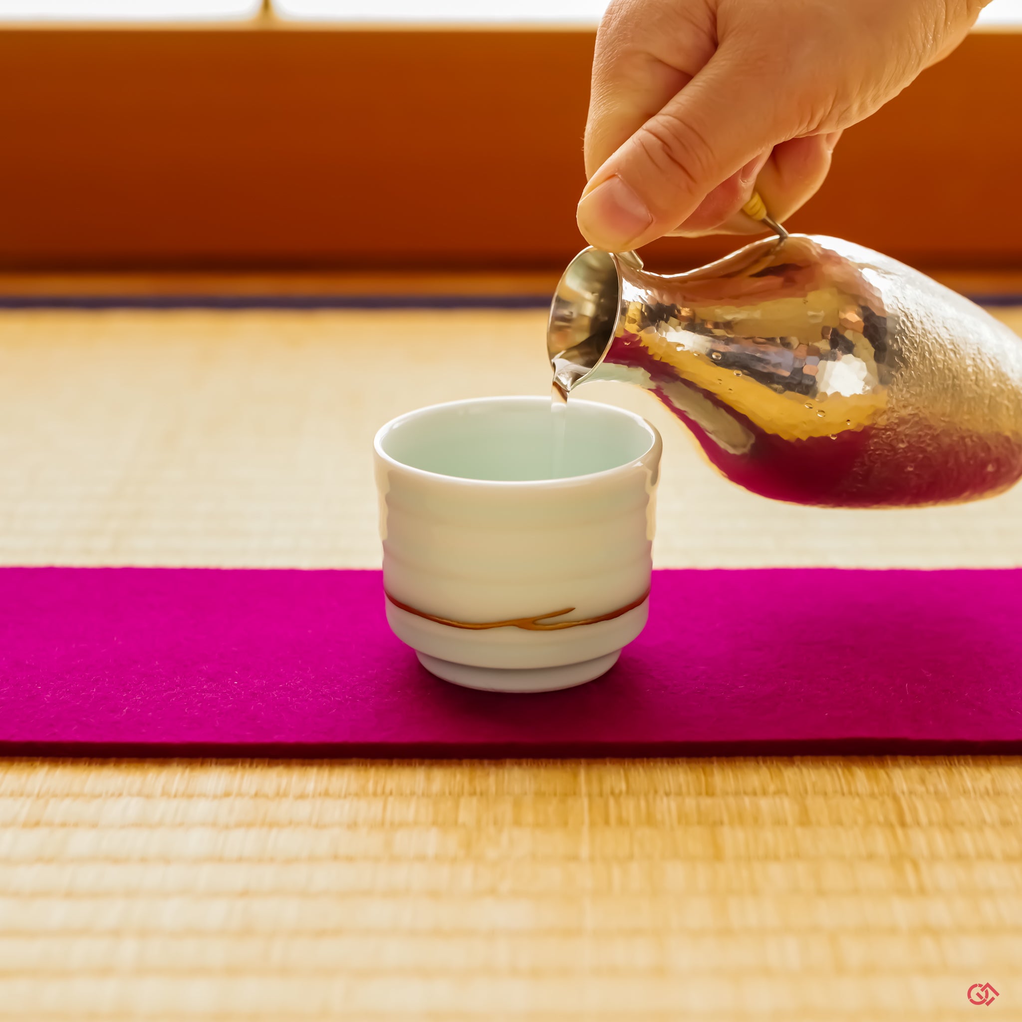 A Kintsugi-repaired vessel rests on a rich purple felt cloth on a tatami mat. Sake is being poured into it from an elegant pewter server, capturing a moment where Japanese heritage and restorative art merge in a beautiful, functional scene.