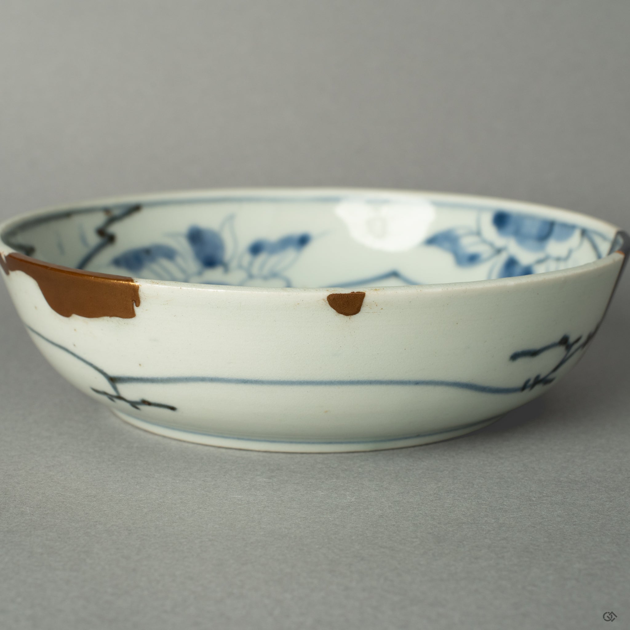A macro view tracing the path of a 24k gold Kintsugi seam as it flows across the historic Ko-Imari porcelain, a testament to its renewed journey.
