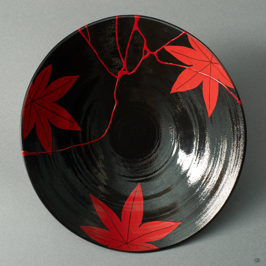 A top-down view of an Arita ware bowl, its black glaze a canvas for the dialogue between crimson maple leaves and vermillion lacquer repair.