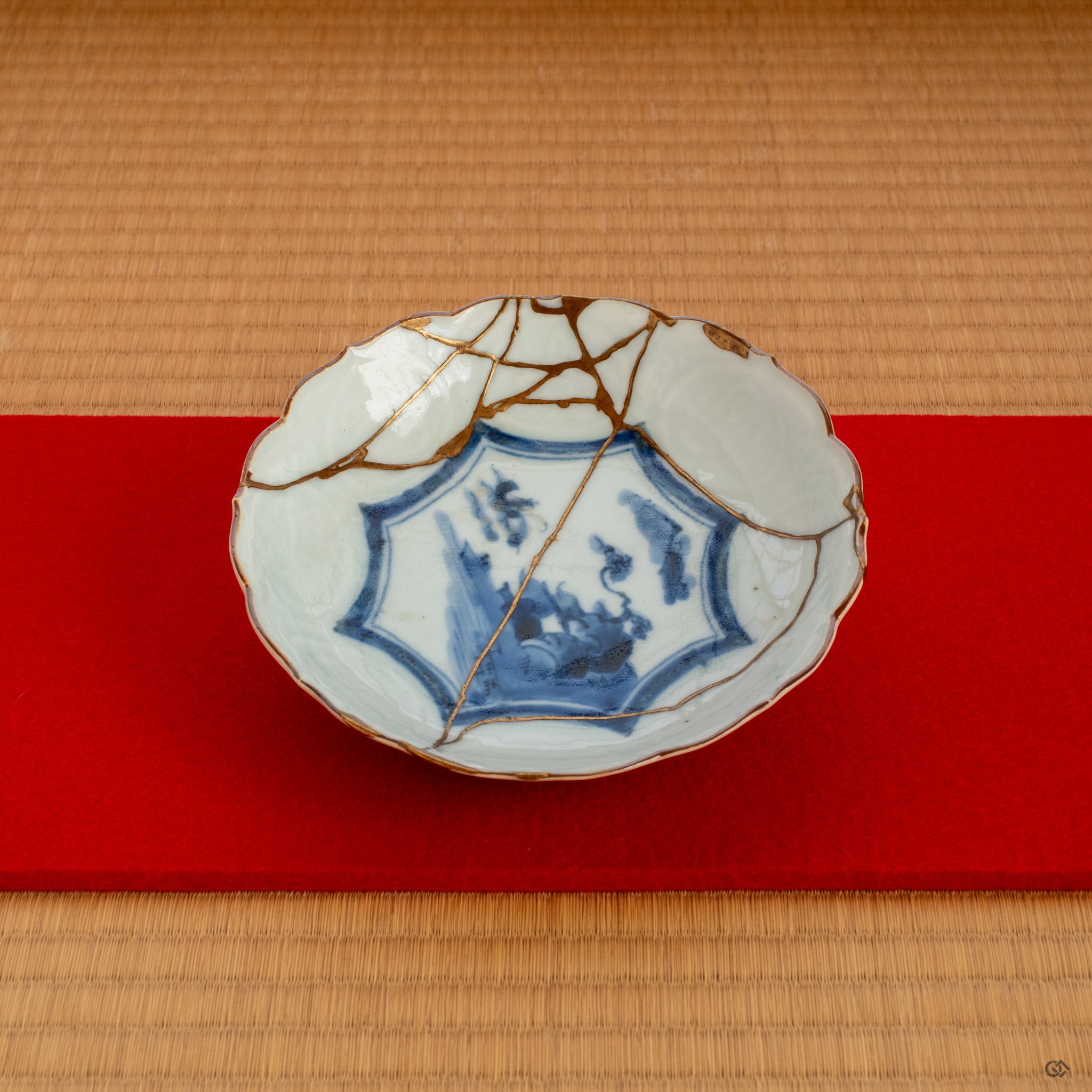 A Ko-Imari kintsugi bowl placed on a red felt cloth, its gold and urushi lacquer repair shining in soft light, inviting a moment of contemplation.