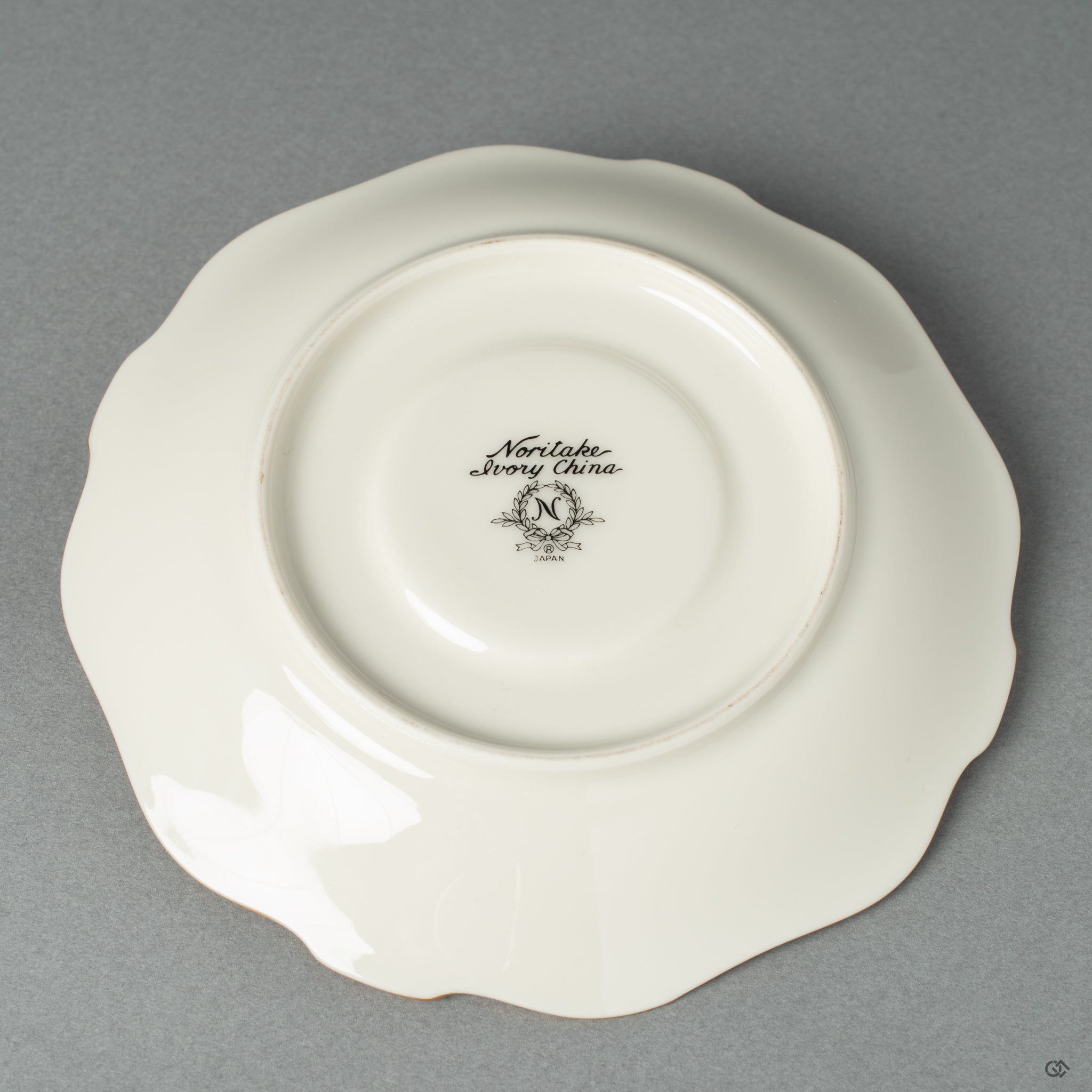 A bottom view of a white Noritake saucer.