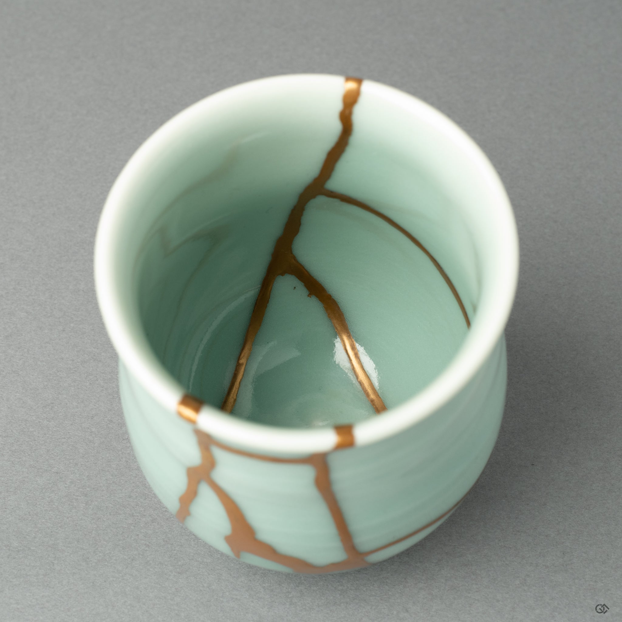 A detail shot focusing on the texture of the 24k gold seam as it meets the fine, glassy celadon glaze of the Nabeshima ware porcelain.