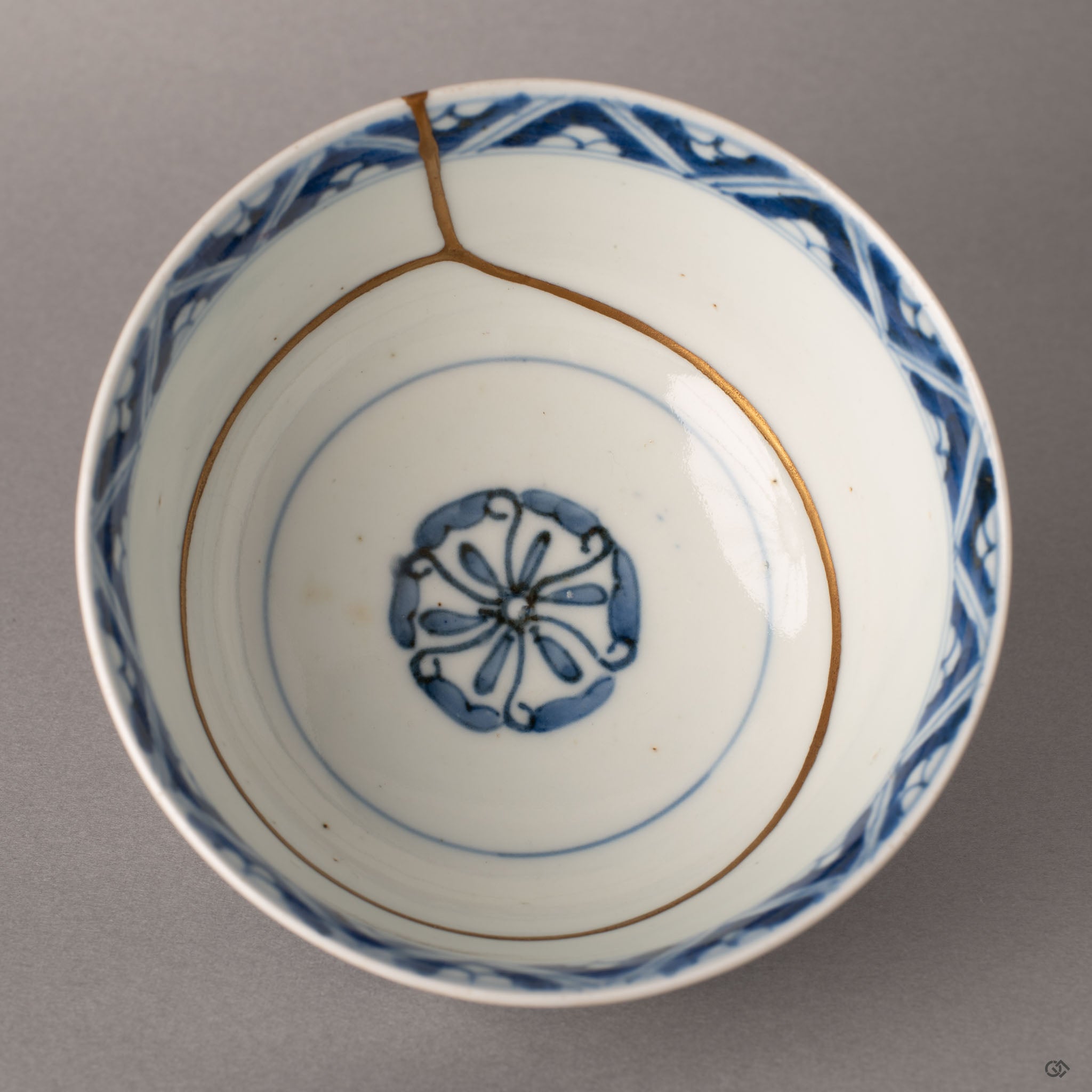 Interior close-up of kintsugi Ko-Imari bowl with gold line tracing across geometric sometsuke blue pattern, crafted resilience in every seam.
