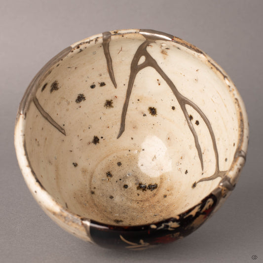 Interior close-up of a kintsugi Shigaraki cup showing silver seams and urushi-e lacquer painting with gestural red and gold strokes over black urushi, a moment of contemplation in lacquer art.