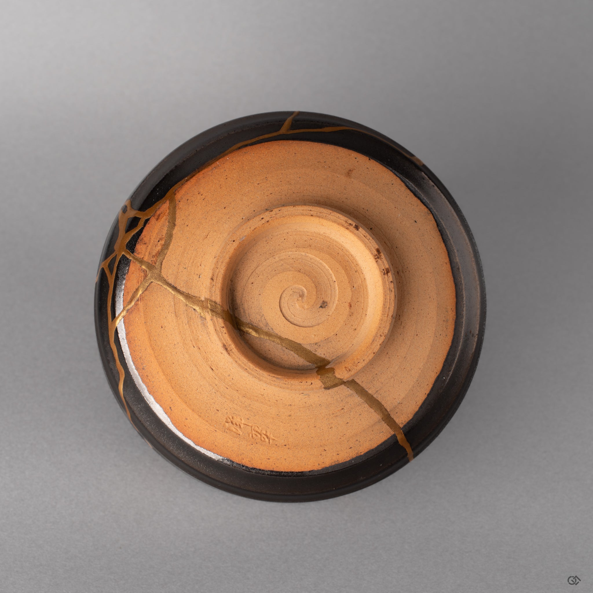 The foot ring of this Arita kintsugi bowl grounds the piece, dark glaze meeting bare clay, history made visible at the base.
