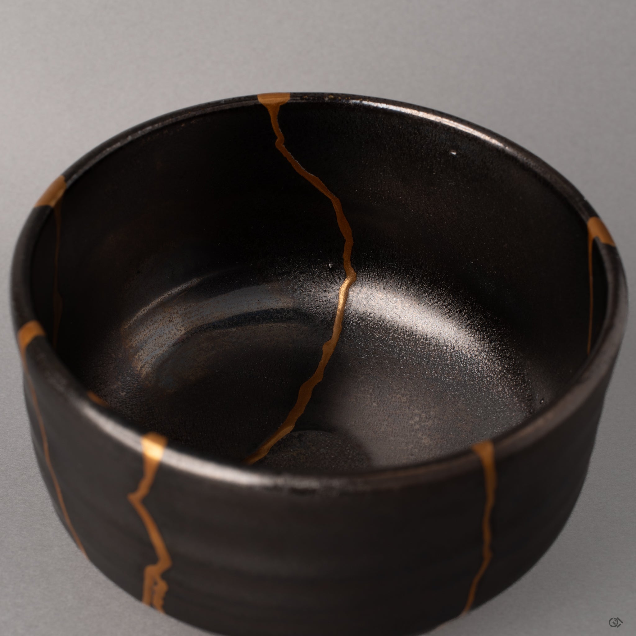 Texture and depth emerge in the kintsugi repair of this gray Arita bowl, urushi layers visible, enduring legacy beneath gold.