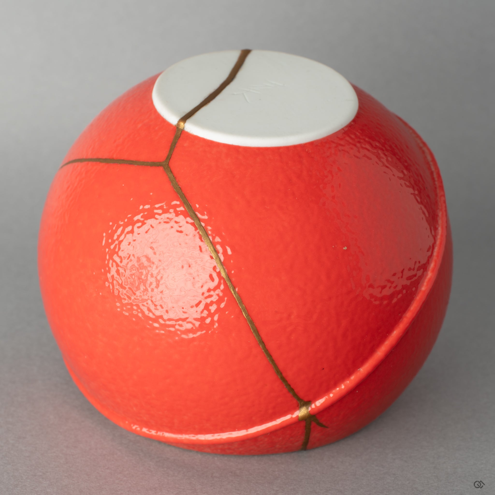 Close-up of the red glaze meeting the gold kintsugi seam, a tactile moment of visible resilience against the smooth surface.