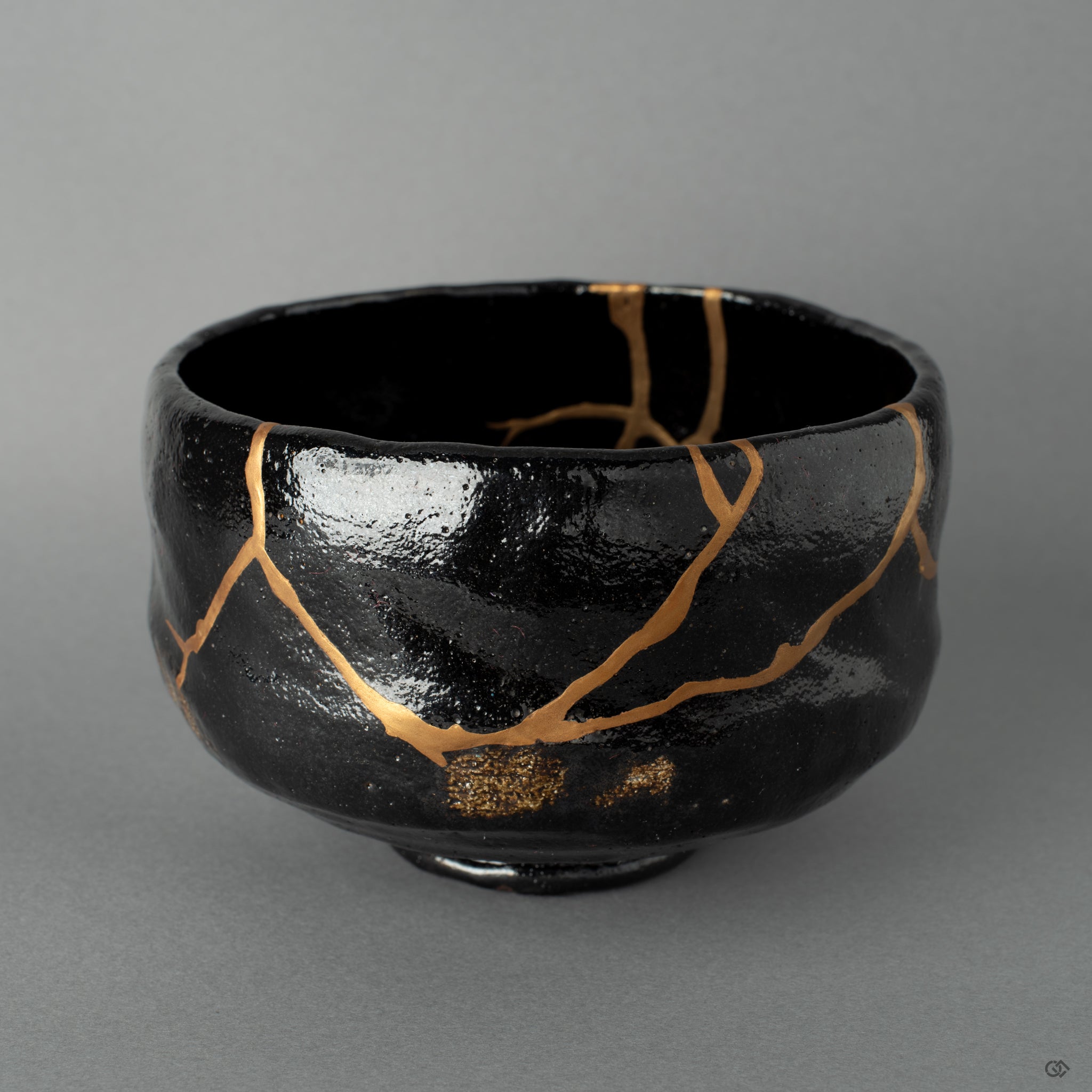 Front view of a Kyoto black matcha bowl restored with kintsugi, burnished gold tracing a quiet beauty across its dark surface.