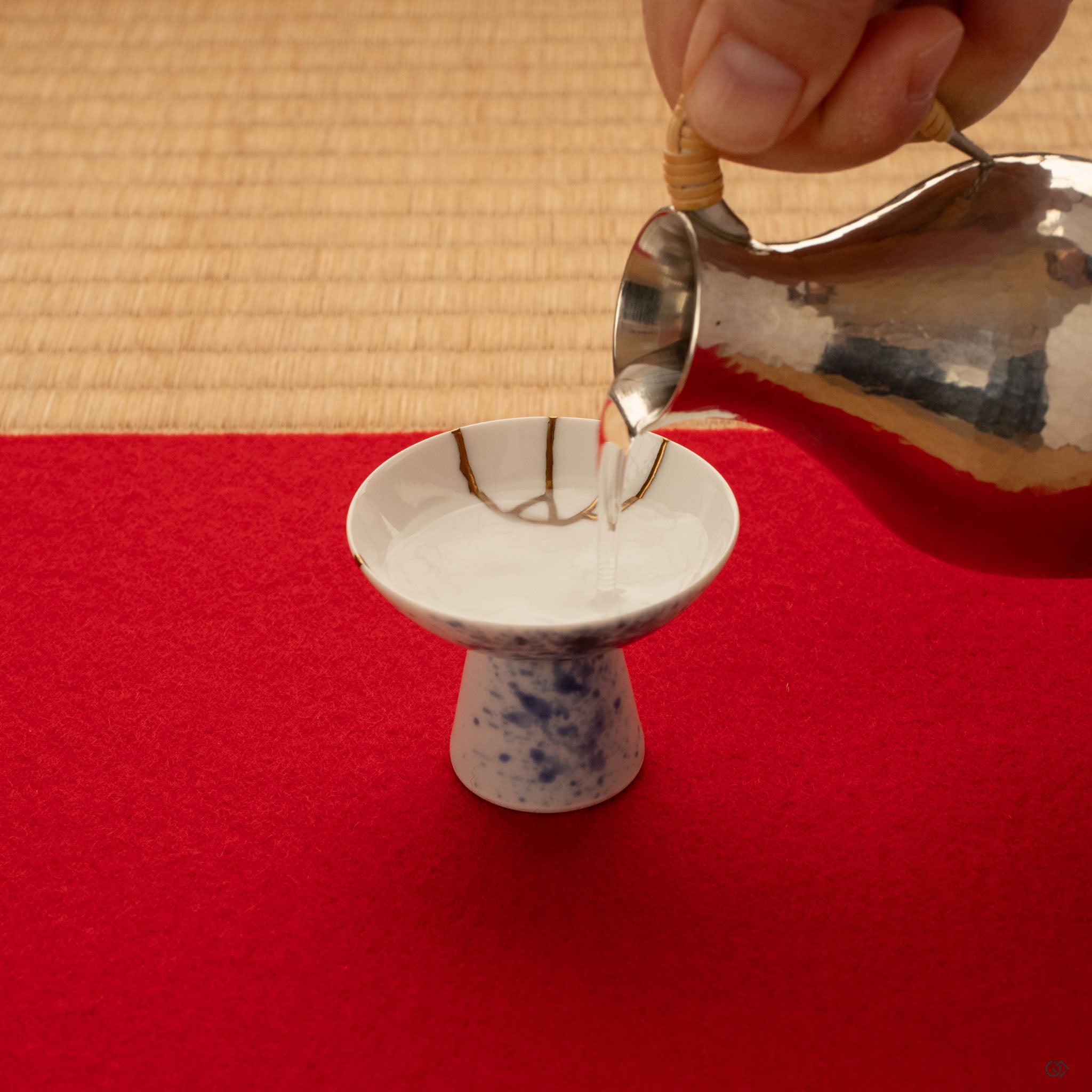Sake poured into a kintsugi Arita cup on tatami, gold seams catching the light over sometsuke blue, functional art with food safety.