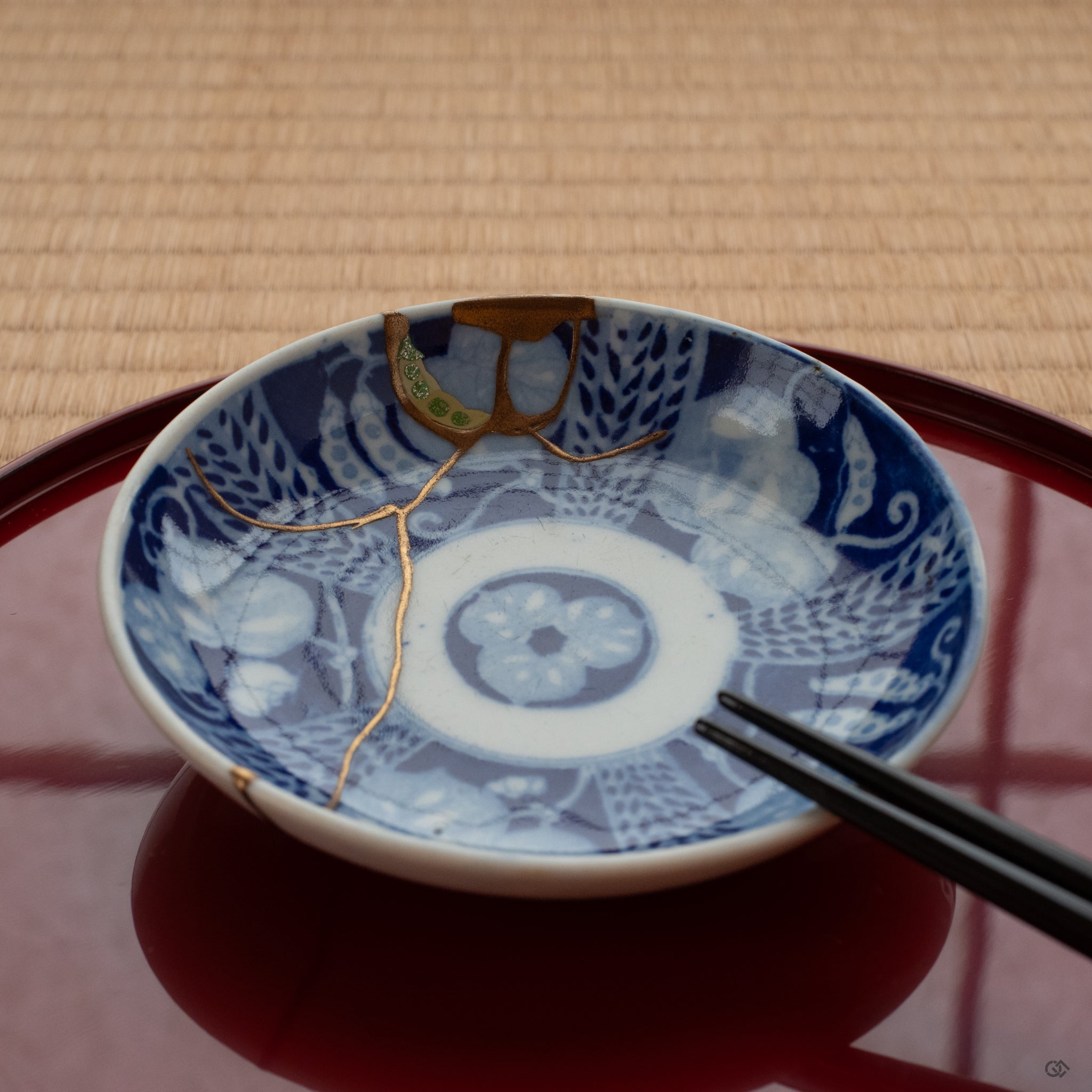 Kintsugi dish on tatami mat, infused with 24k gold and urushi, embodying a moment of contemplation in a tea room setting.