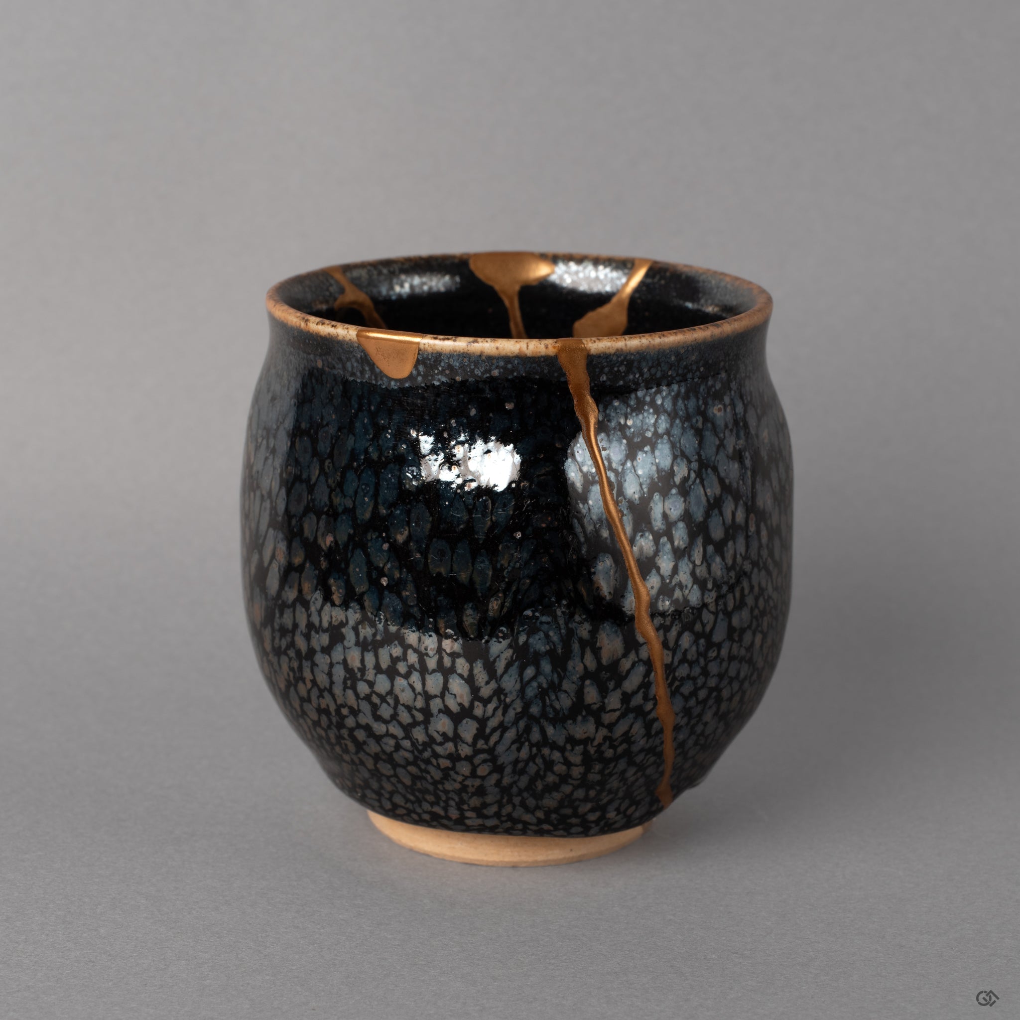 Silver flecks scatter across the tenmoku surface like distant stars, kintsugi gold crossing between, beauty in imperfection up close.