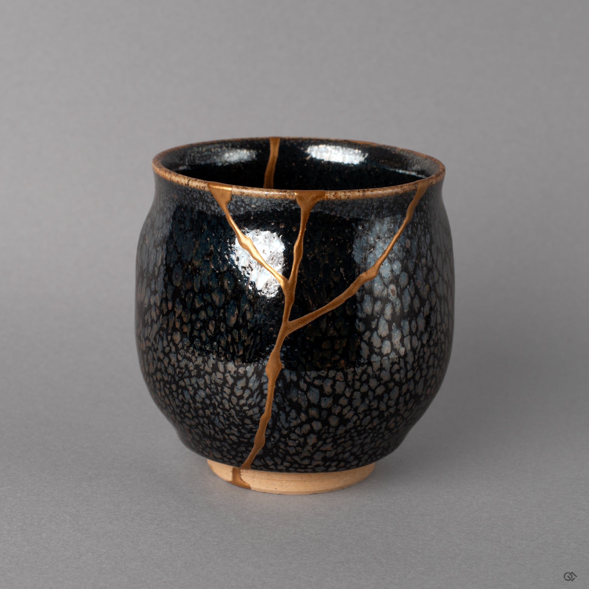 Tenmoku Kyoto tea cup with silver star-like glaze, kintsugi seams in 24K gold threading through, wabi-sabi written in kiln fire.