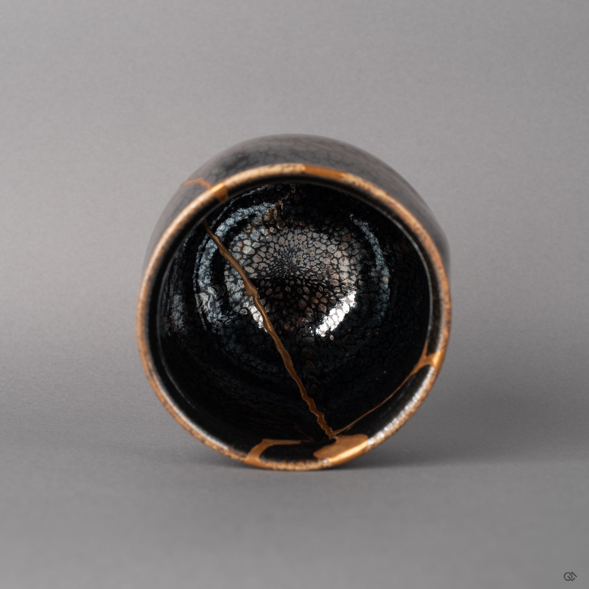 From above, the tenmoku cup reveals scattered silver flecks and kintsugi lines descending inward, a quiet beauty in the round.