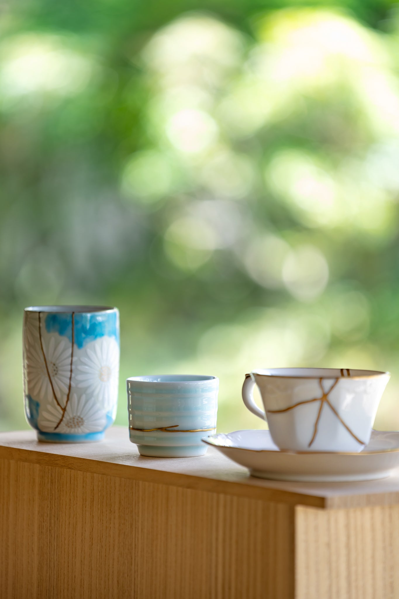 Authentic Kintsugi pottery set with 24k gold restoration, featuring a teacup, sake cup, and saucer on a Japanese paulownia shelf.