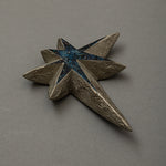 Three-quarter view of Keiko Hata's Kiraboshi / Hakugin (Glittering Stars · Silver, 2024): a multi-pointed star with textured silver tin-powder rays surrounding a blue-black urushi (Japanese lacquer) core inlaid with glittering raden (mother-of-pearl).