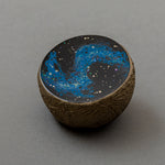 Angled view of Keiko Hata's Union of Skies (2024): a domed black urushi (Japanese lacquer) center with blue raden (mother-of-pearl) inlay, cradled in a pale gilded ring finished with water gold leaf.