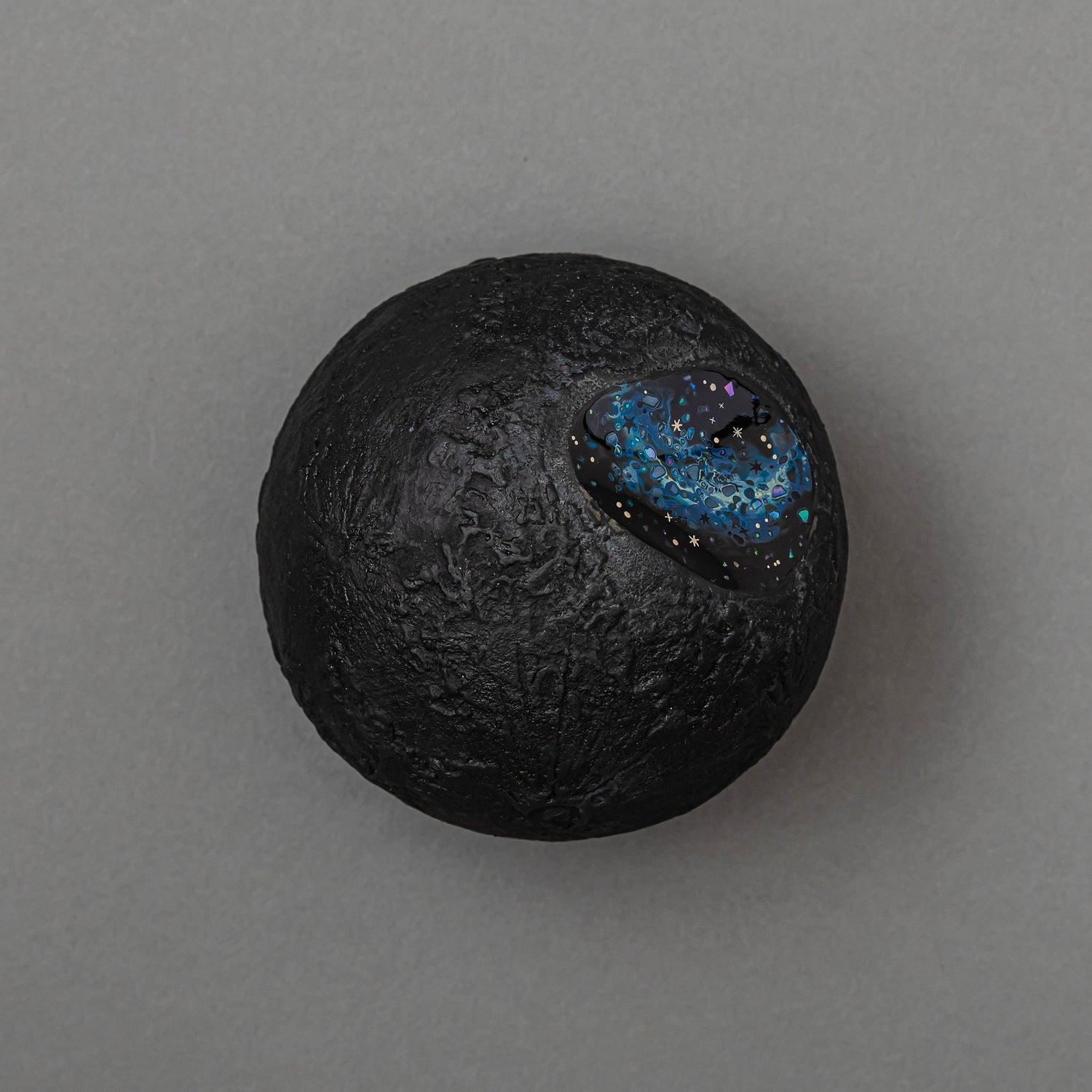 Top view of Keiko Hata's Amamitsuki (Full Moon of the Heavens, 2024) mounted on a round dark wood panel: a textured gold-leaf urushi (Japanese lacquer) moon set with an oval blue raden (mother-of-pearl) window of stars.