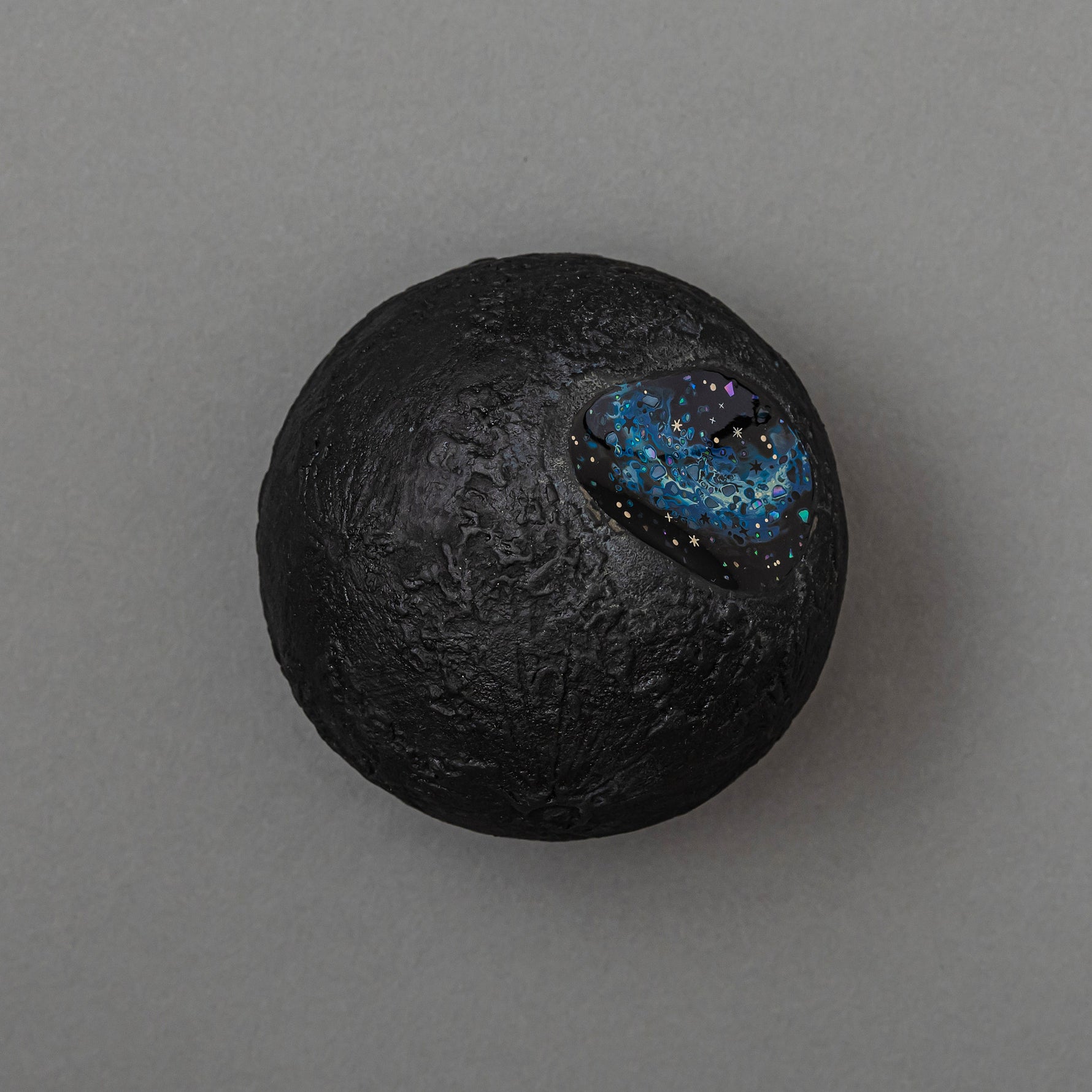 Top view of Keiko Hata's Amamitsuki (Full Moon of the Heavens, 2024) mounted on a round dark wood panel: a textured gold-leaf urushi (Japanese lacquer) moon set with an oval blue raden (mother-of-pearl) window of stars.