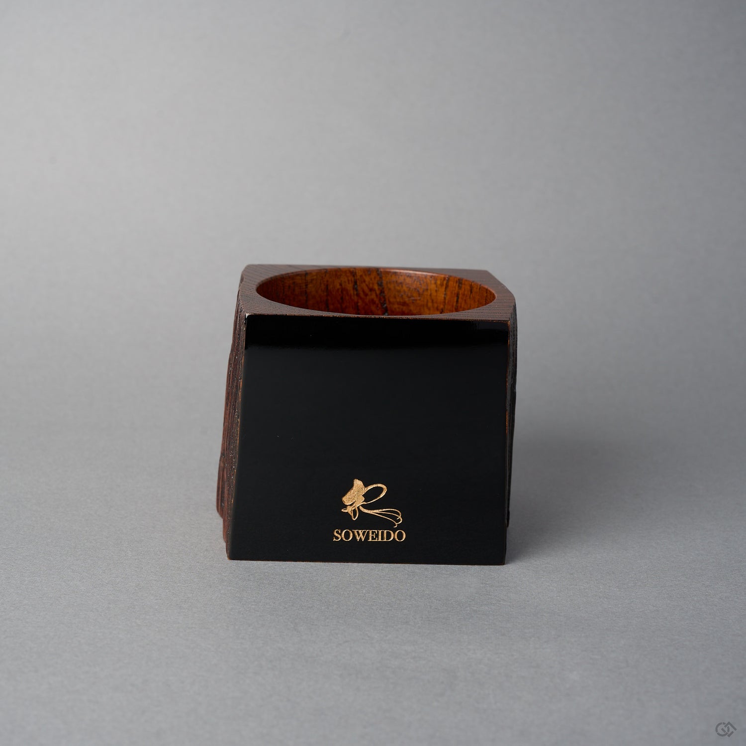 Angled front view of Nobuyasu Suginaka's KODAMA Black Roiro (2024): a roughly square aged-wood vessel whose front face is finished in mirror-polished jet-black urushi lacquer bearing a gold SOWEIDO logo.