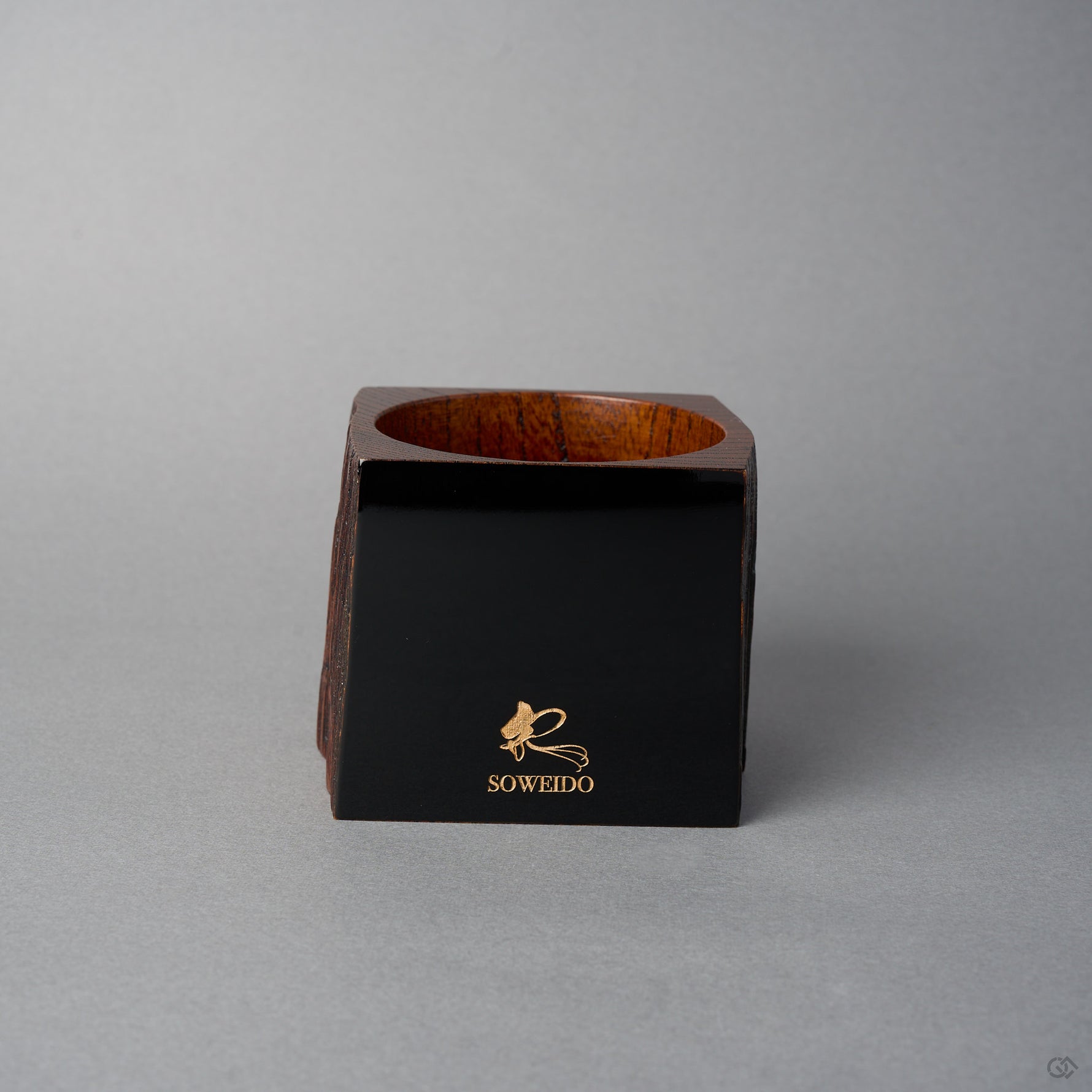 Angled front view of Nobuyasu Suginaka's KODAMA Black Roiro (2024): a roughly square aged-wood vessel whose front face is finished in mirror-polished jet-black urushi lacquer bearing a gold SOWEIDO logo.
