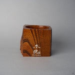 Angled front view of Nobuyasu Suginaka's KODAMA Fuki-urushi : a keyaki (zelkova) wood vessel whose front face is finished in wiped lacquer that brings out the natural grain, engraved with a silver KODAMA logo.