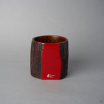 Angled front view of Nobuyasu Suginaka's KODAMA Red Roiro: an aged-wood vessel whose flat front face is finished in mirror-polished crimson urushi lacquer, marked with a gold logo.