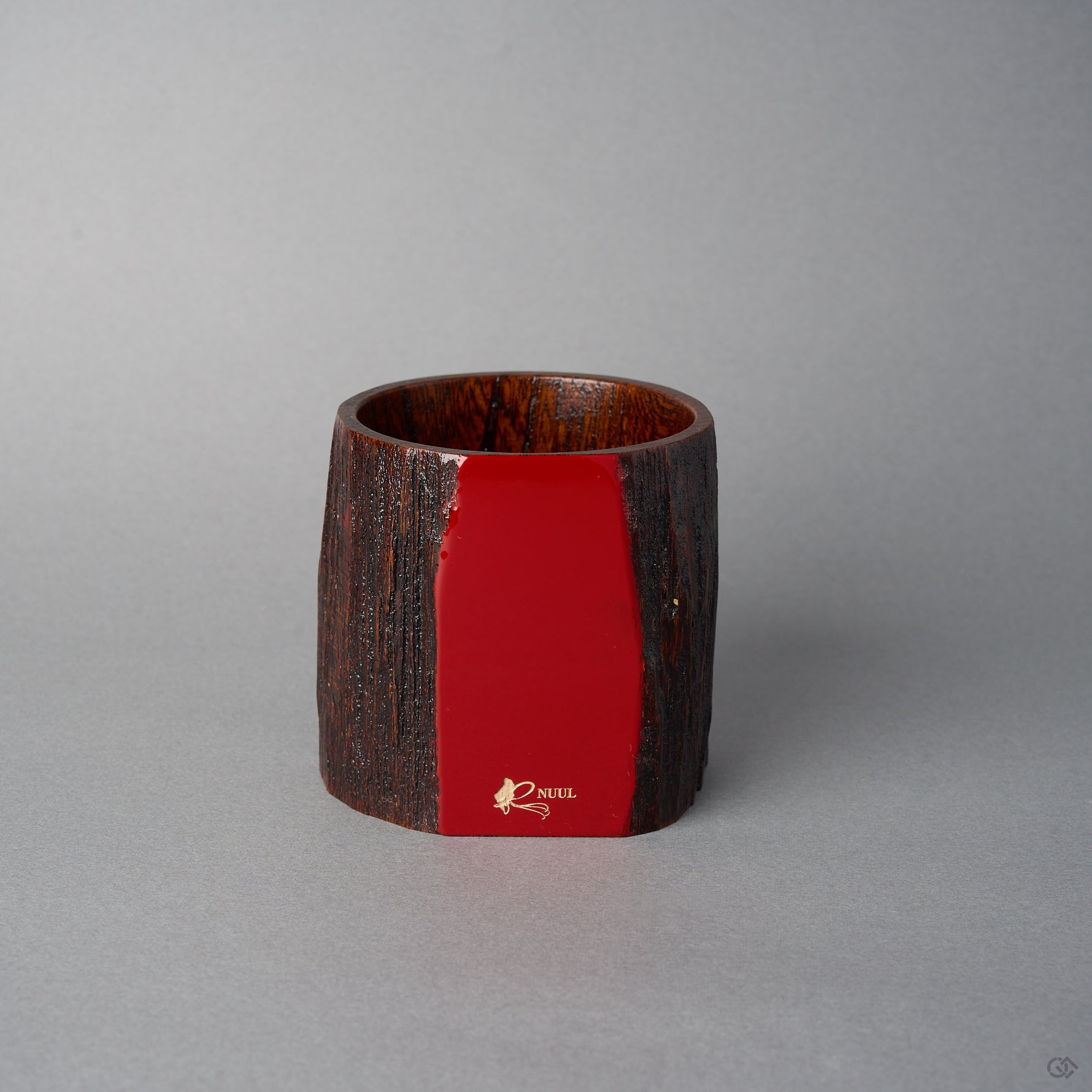 Angled front view of Nobuyasu Suginaka's KODAMA Red Roiro: an aged-wood vessel whose flat front face is finished in mirror-polished crimson urushi lacquer, marked with a gold logo.