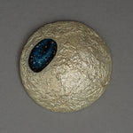 The gilded moon of Amamitsuki by Keiko Hata seen from above, its cratered gold-leaf surface holding an oval blue raden window scattered with starlike flecks.