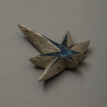 Angled view of Kiraboshi / Hakugin by Keiko Hata, showing the long pointed rays of the silver star and its starry blue raden center catching the light.