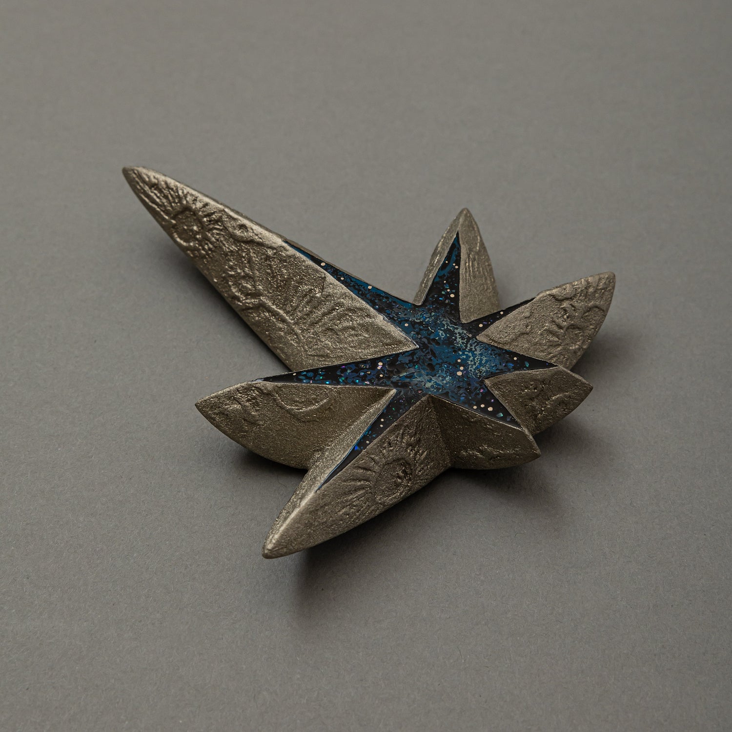 Angled view of Kiraboshi / Hakugin by Keiko Hata, showing the long pointed rays of the silver star and its starry blue raden center catching the light.