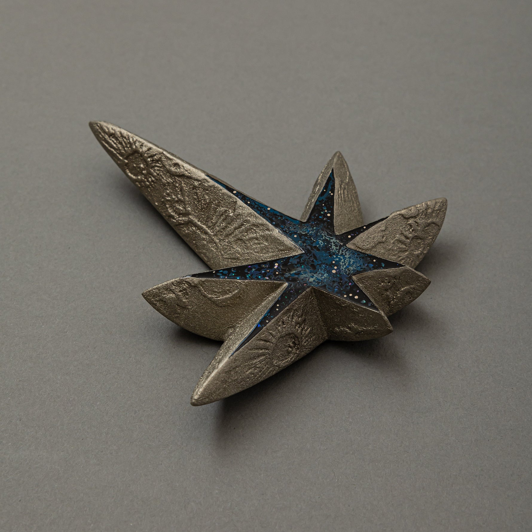 Angled view of Kiraboshi / Hakugin by Keiko Hata, showing the long pointed rays of the silver star and its starry blue raden center catching the light.