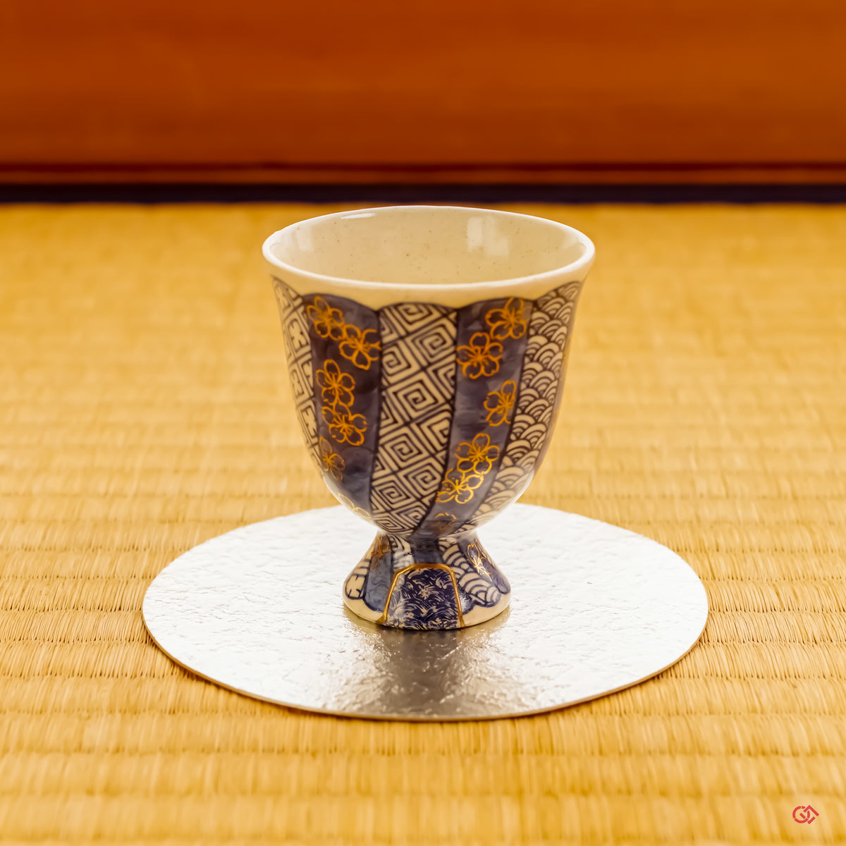 A beautifully restored Kintsugi vessel from Kyoto, resting on a lustrous, thin pewter coaster atop a traditional tatami mat. The scene captures a serene harmony between historic craft and modern elegance.