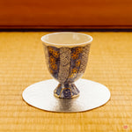 A beautifully restored Kintsugi vessel from Kyoto, resting on a lustrous, thin pewter coaster atop a traditional tatami mat. The scene captures a serene harmony between historic craft and modern elegance.