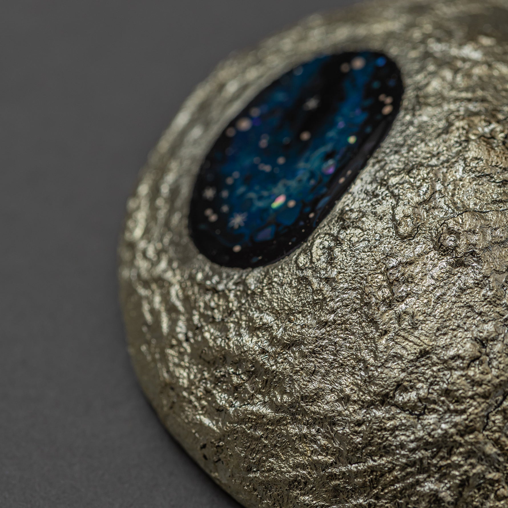 Angled detail of Amamitsuki, showing the domed gold-leaf surface and the blue raden window where iridescent flecks glitter like stars against the dark lacquer.