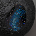 Angled detail of Amamitsuki, showing the domed gold-leaf surface and the blue raden window where iridescent flecks glitter like stars against the dark lacquer.