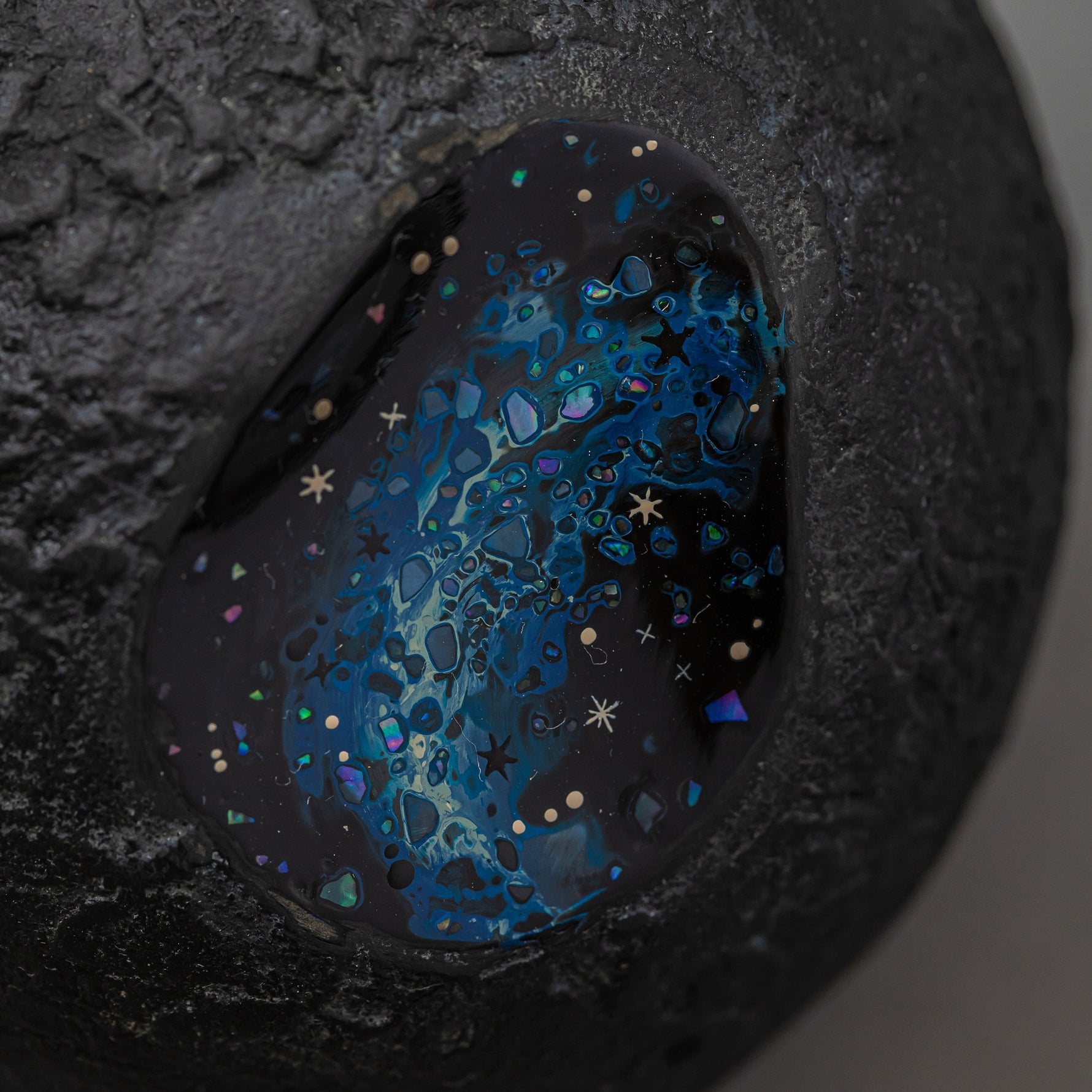 Angled detail of Amamitsuki, showing the domed gold-leaf surface and the blue raden window where iridescent flecks glitter like stars against the dark lacquer.
