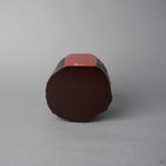 Base view of KODAMA Red Roiro, showing the rounded end-grain bottom of the aged wood and the crimson lacquer face with its gold logo along the edge.