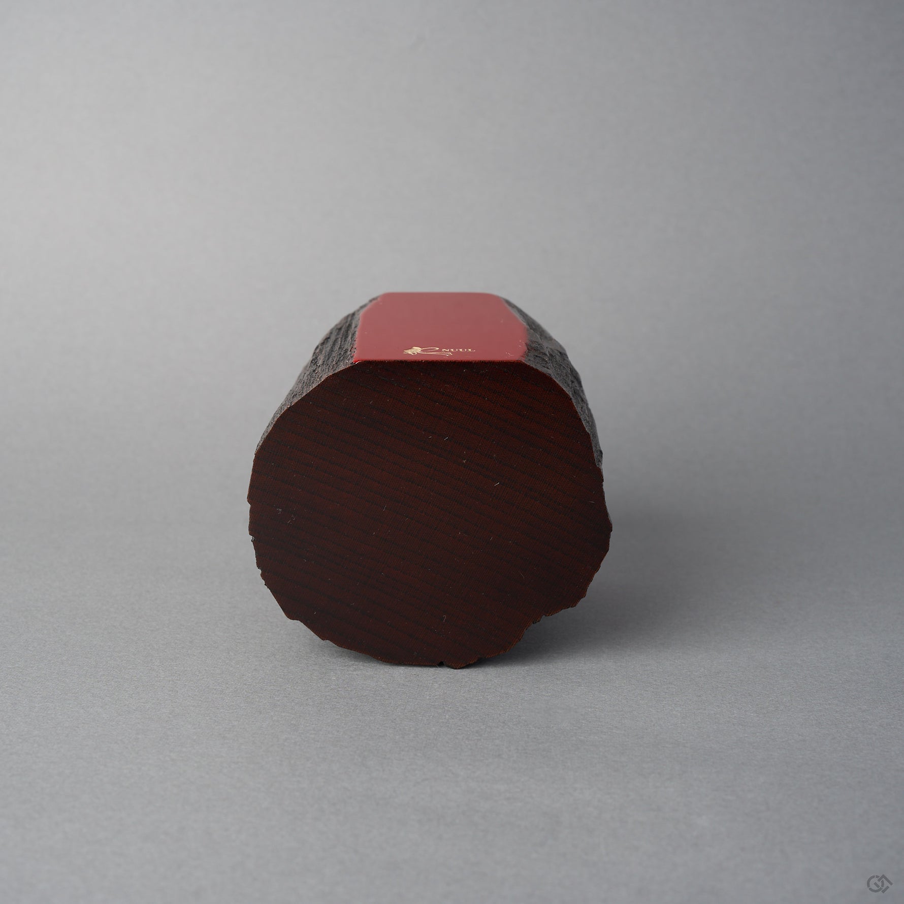 Base view of KODAMA Red Roiro, showing the rounded end-grain bottom of the aged wood and the crimson lacquer face with its gold logo along the edge.