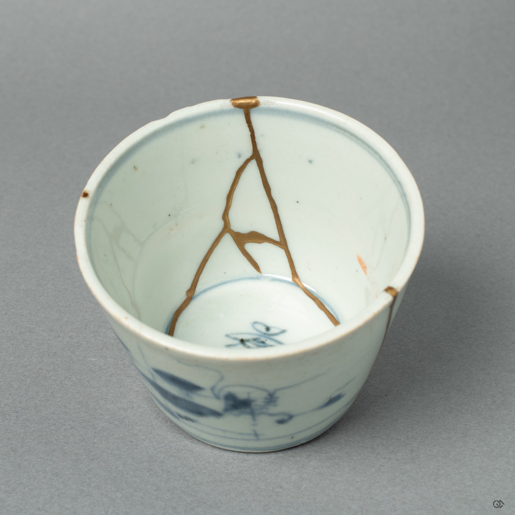 A detailed close-up of a 24k gold Kintsugi line on the antique Ko-Imari porcelain. The precision reflects the meticulous skill honed through the restoration of sacred sculptures.
