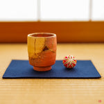 A beautifully restored Kintsugi teacup resting on a lustrous, thin pewter coaster atop a traditional tatami mat. The tranquil scene captures a harmony between historic Japanese craft and refined, contemporary elegance.