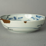 A macro view tracing the path of a 24k gold Kintsugi seam as it flows across the historic Ko-Imari porcelain, a testament to its renewed journey.