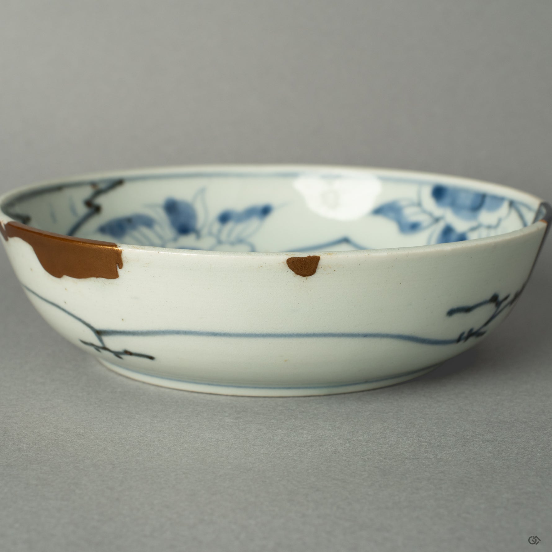 A macro view tracing the path of a 24k gold Kintsugi seam as it flows across the historic Ko-Imari porcelain, a testament to its renewed journey.