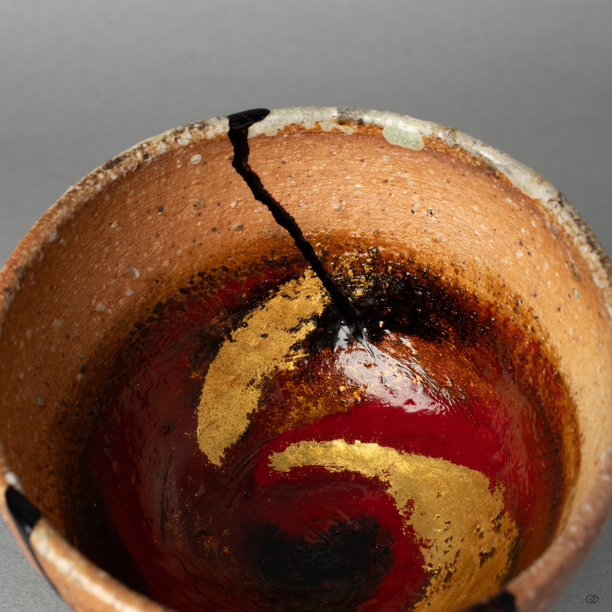 A detailed close-up of the gold leaf (haku-e) and colored lacquer on the rustic clay, making the vessels history made visible in a new form.